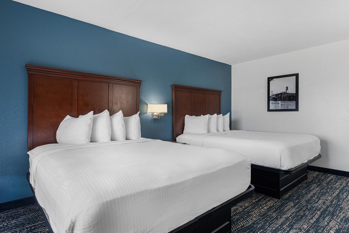 Une chambre d’hôtel avec deux lits, un mur d’accent bleu, un tableau encadré au mur et un sol recouvert de moquette.