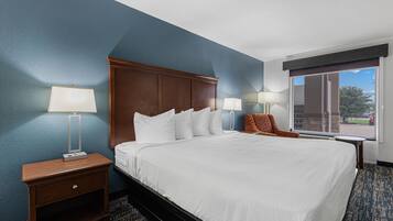 Quarto de hotel com uma cama grande, duas mesas de cabeceira com luminárias, uma cadeira e vista para o exterior.