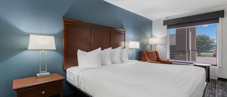 A hotel room with a large bed, two bedside tables with lamps, a chair, and a view of the outdoors.