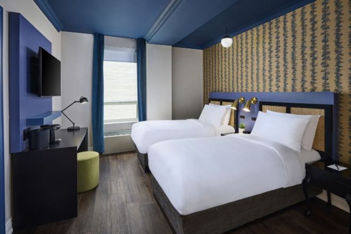 A hotel room with two beds, a desk, a TV, and a window with curtains.