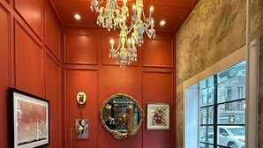 A room with a red wall, a large chandelier, a sofa, two chairs, a coffee table, and a view of the street through a window. - Hotel Victoria (Toronto)