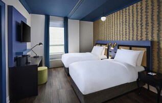 Hotelkamer met twee bedden, een flatscreen-tv, een bureau met lamp en een raam met gordijnen.