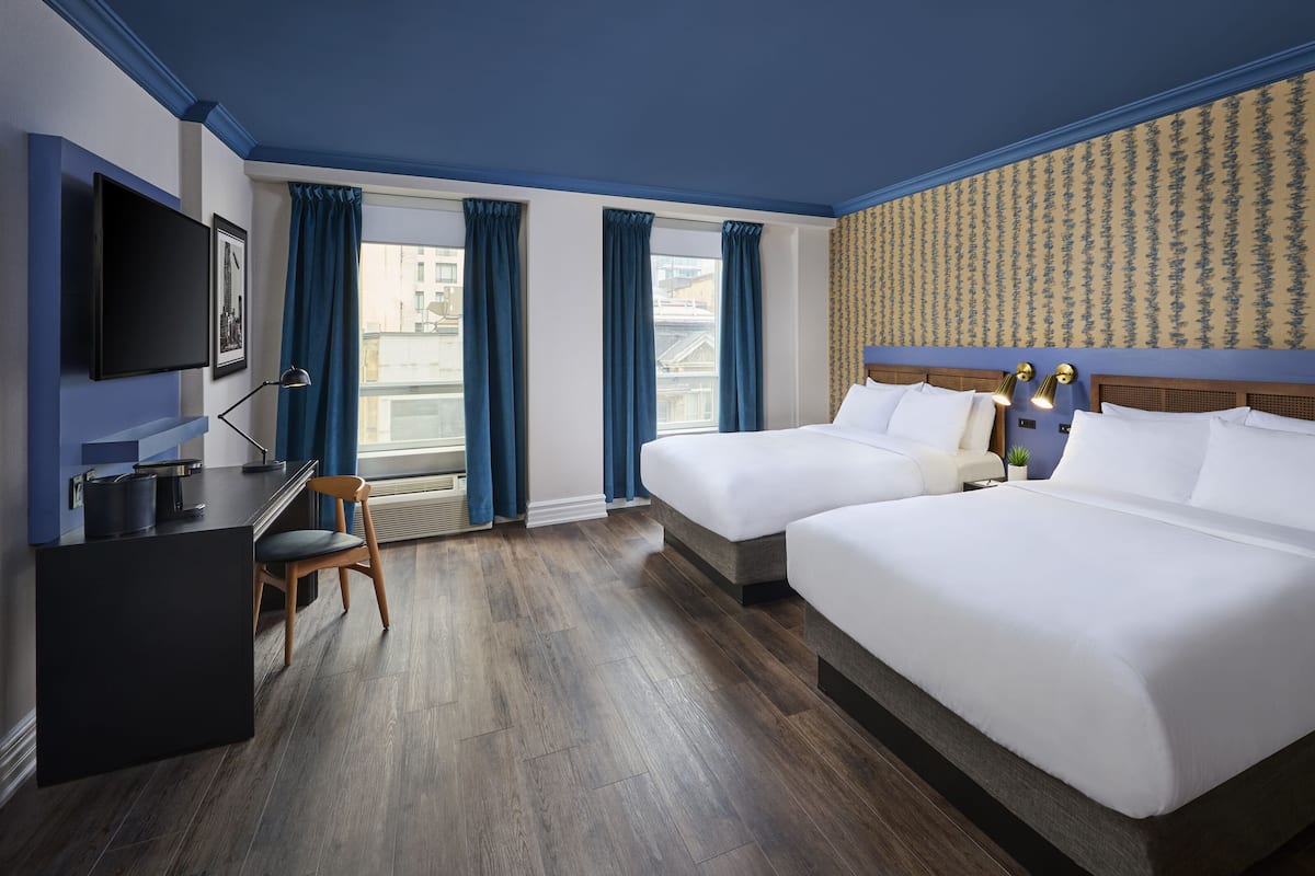 A hotel room with two beds, a desk, a chair, a TV, and a window with curtains.