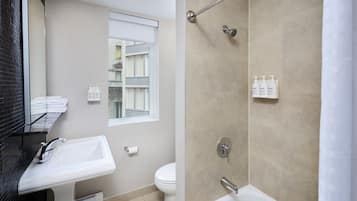 A modern bathroom with a bathtub, toilet, and sink. There is a window with a view of buildings outside.