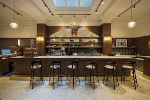 A bar area with a central counter, multiple stools, and a variety of coffee-making equipment.