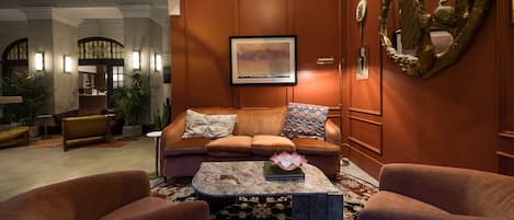 A lobby with a brown leather sofa, two armchairs, a marble coffee table, and a framed painting on the wall.