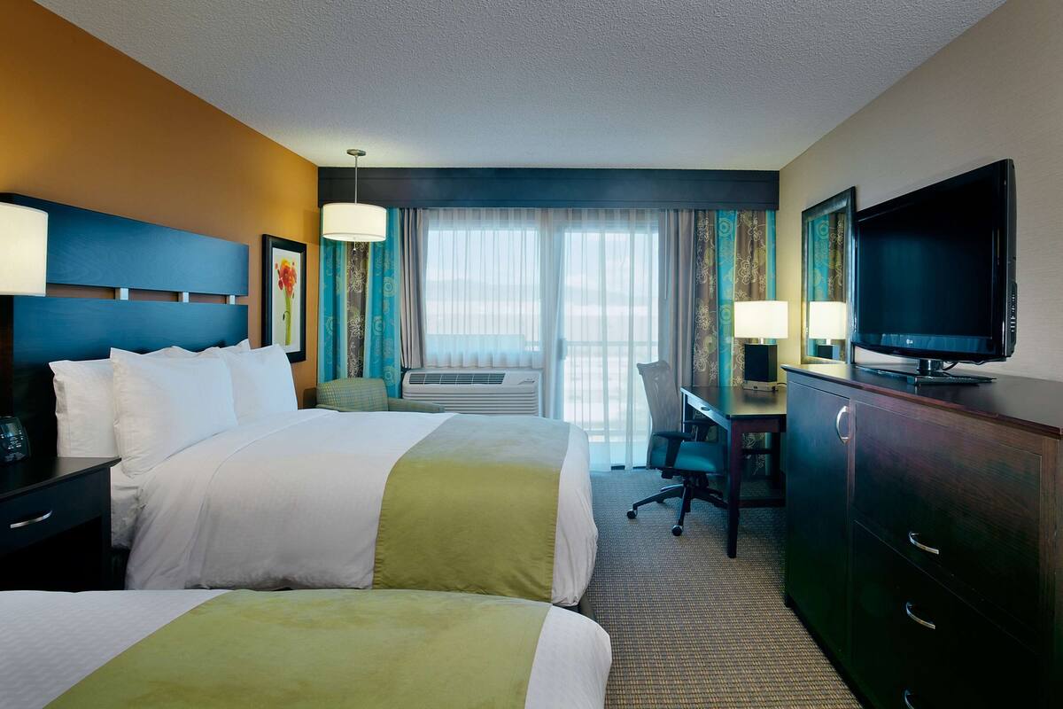 A hotel room with two beds, a desk, a television, and a window with curtains.