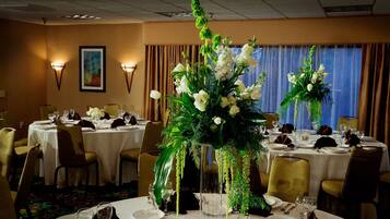 Comedor con mesas redondas dispuestas para una comida, con manteles blancos, centros de mesa florales y sillas doradas.