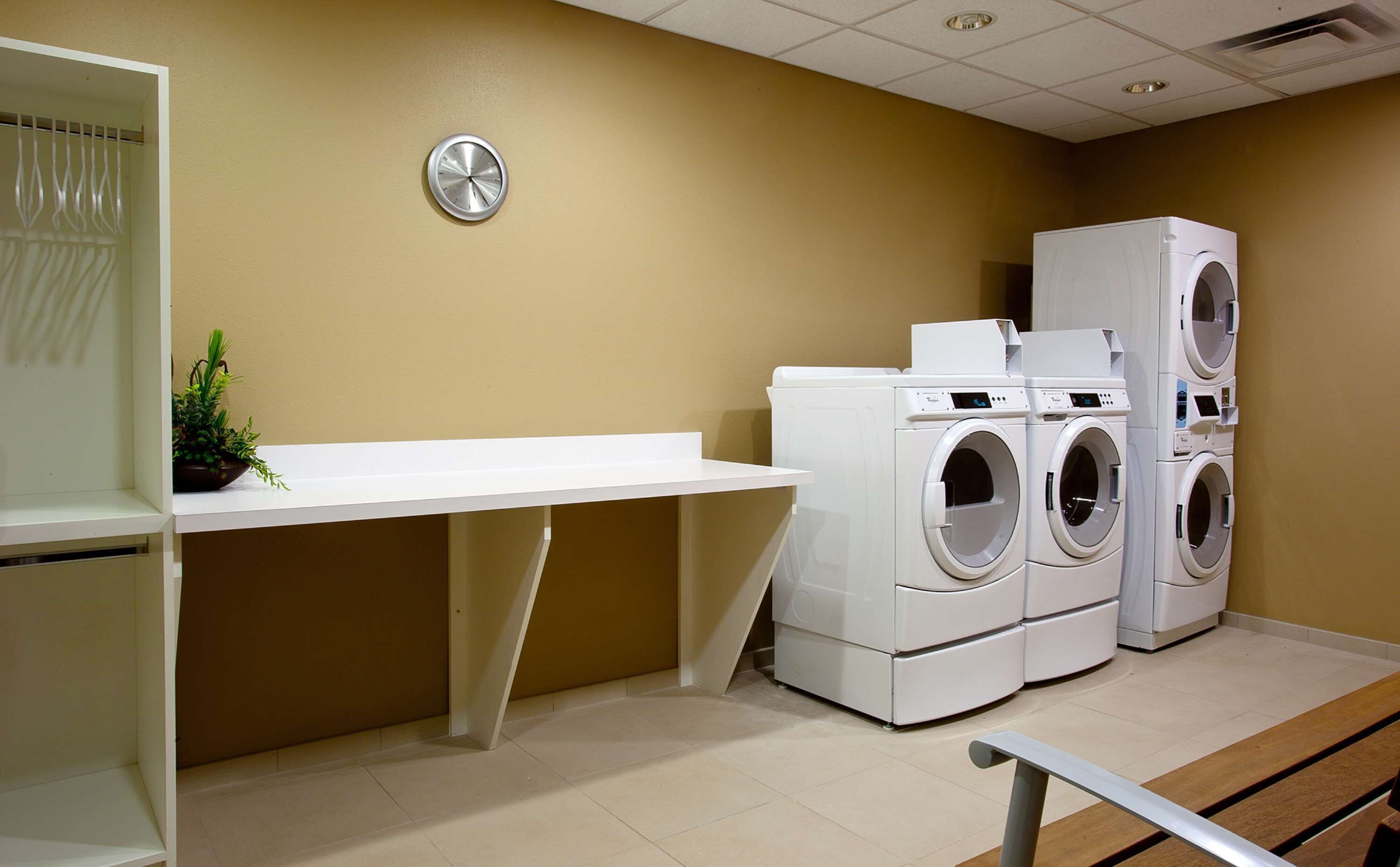 A laundry room with a white sink, a clock on the wall, and three stacked front-loading washing machines.