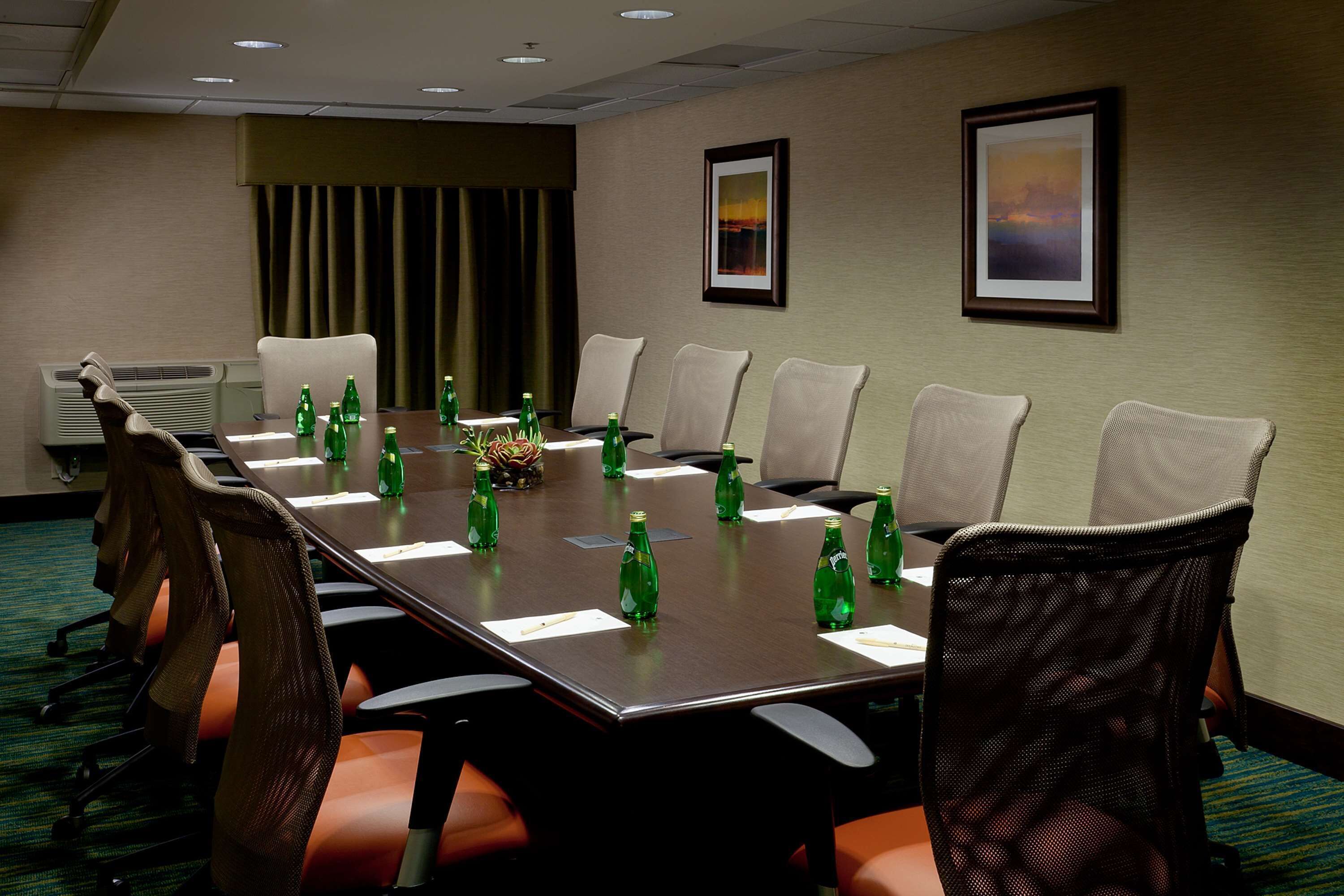 A conference room with a long table, chairs, and green bottles on the table.