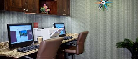 Ein Hotelbüro mit zwei Computertischen, zwei Stühlen, einer Uhr und Holzausbau.