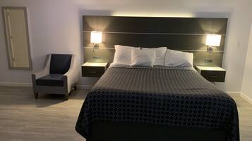 A modern hotel room with a large bed, two bedside tables with lamps, a chair, and a mirror on the wall.