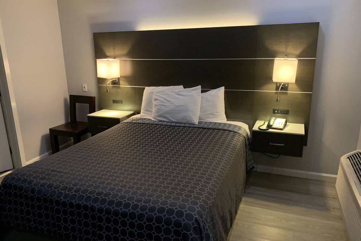 A hotel room with a large bed, two bedside tables, a nightstand, and a wall-mounted phone.