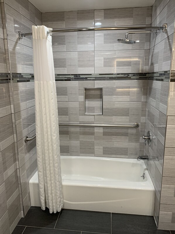 A modern shower area with a glass-enclosed tub, a handrail, and a showerhead.