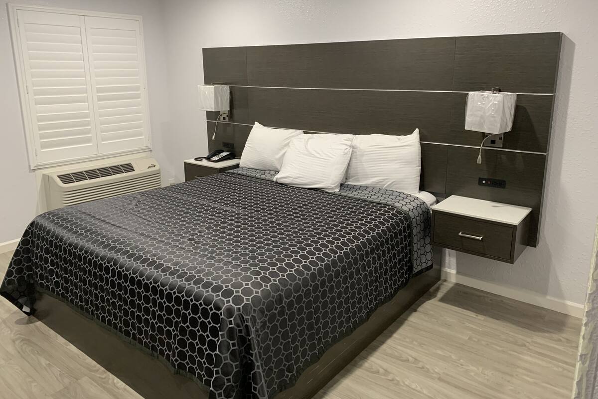 A modern hotel room with a large bed, a bedside table with a phone, and a nightstand.