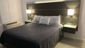 A neatly made bed with a dark patterned bedspread, two bedside lamps, a nightstand with a phone, and a wall-mounted light fixture.
