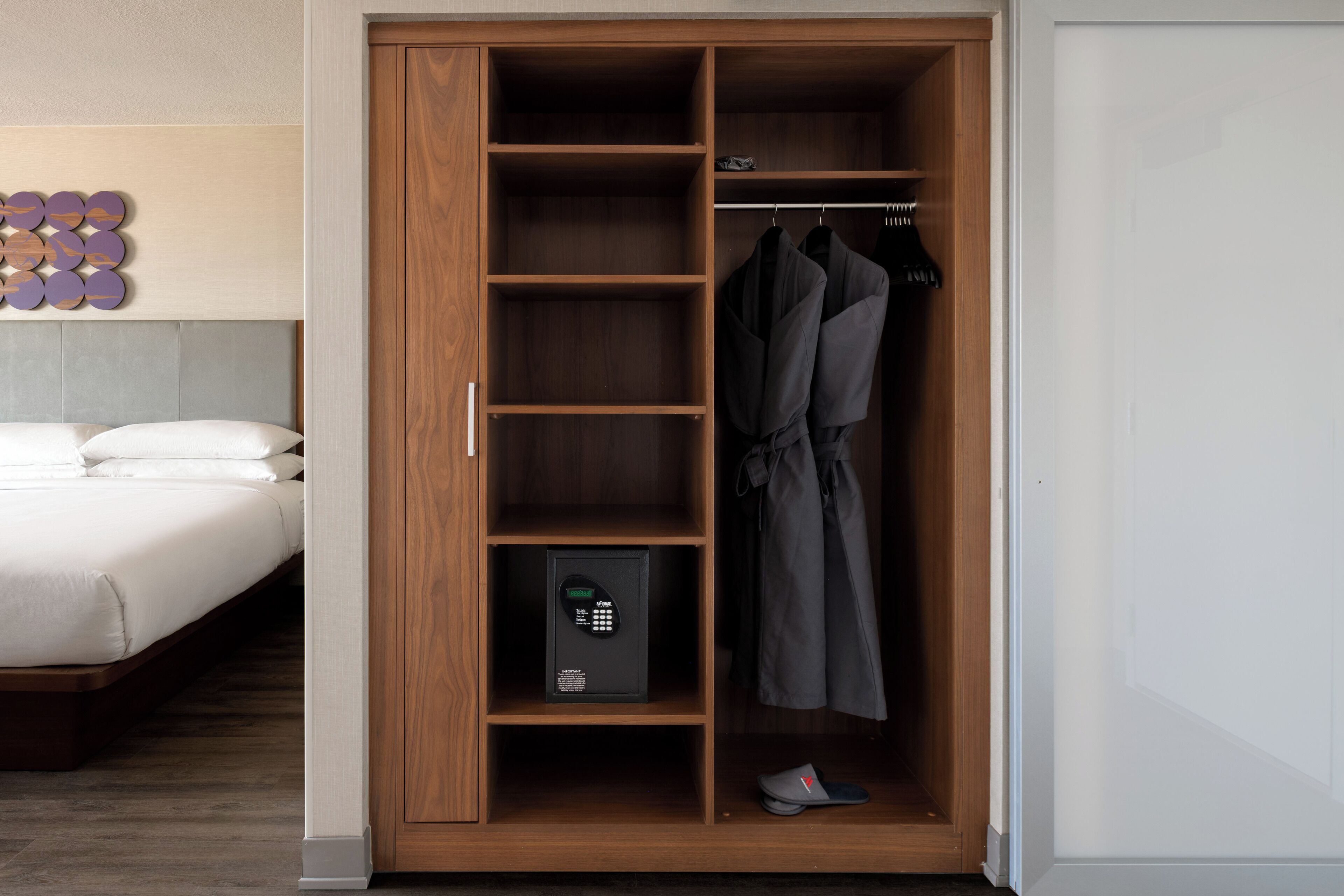A bedroom with a wooden wardrobe, a bed, and a shoe rack.