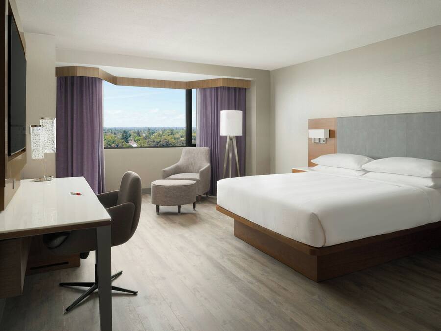 A hotel room with a large bed, a desk, a chair, a lamp, and a view of the outdoors.