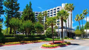 A hotel with a modern design, featuring a central courtyard with palm trees and flower beds, surrounded by tall buildings.