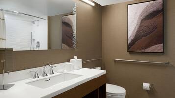 A modern bathroom with a large mirror, a sink with two faucets, a toilet, and a towel rack.