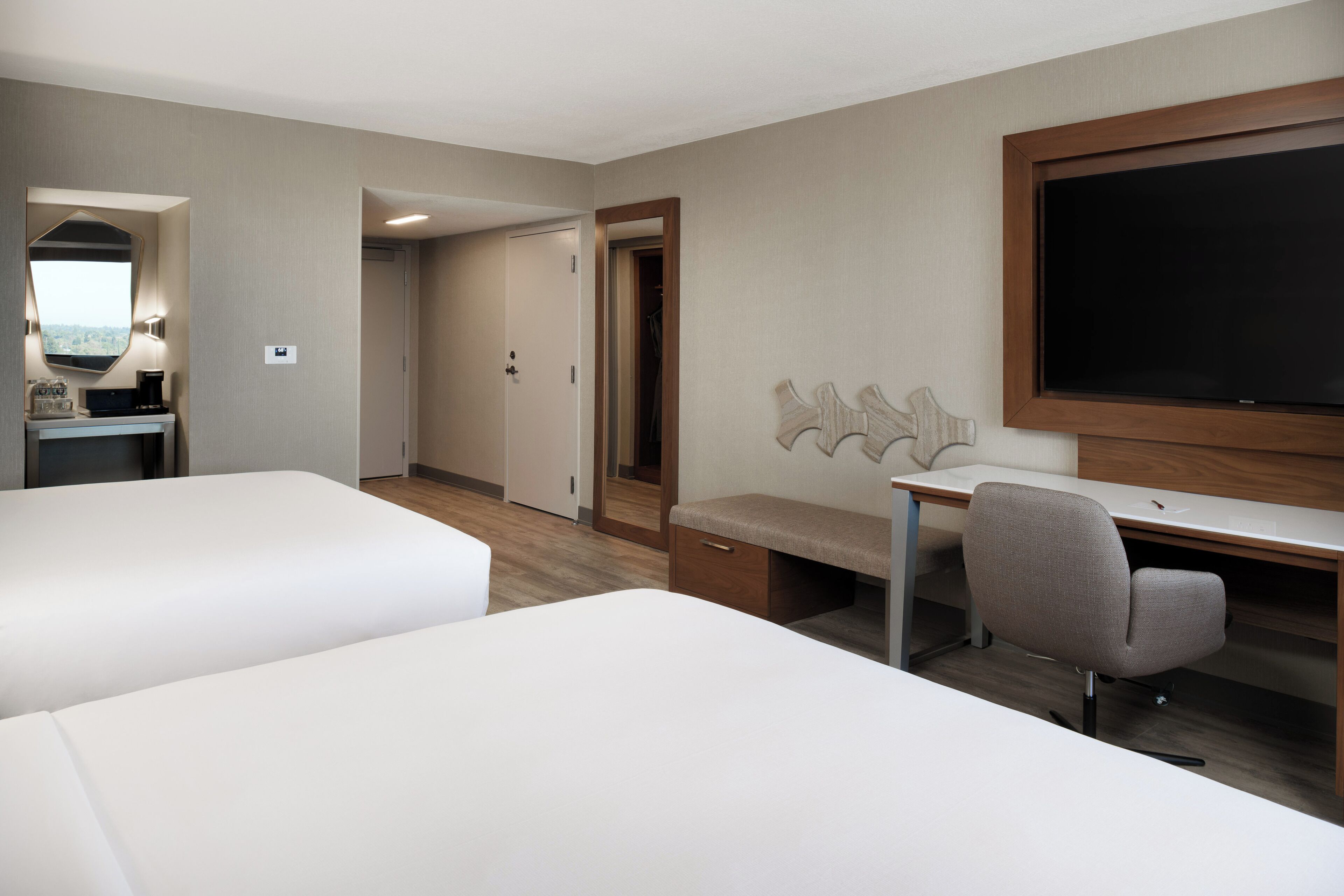 Quarto de hotel com duas camas, uma escrivaninha, uma cadeira, uma televisão e um espelho.