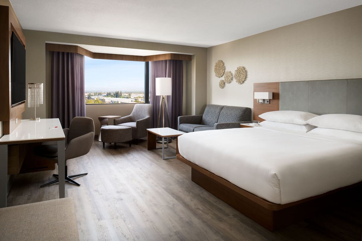 A hotel room with a large bed, a desk, a chair, a sofa, and a view of the city.