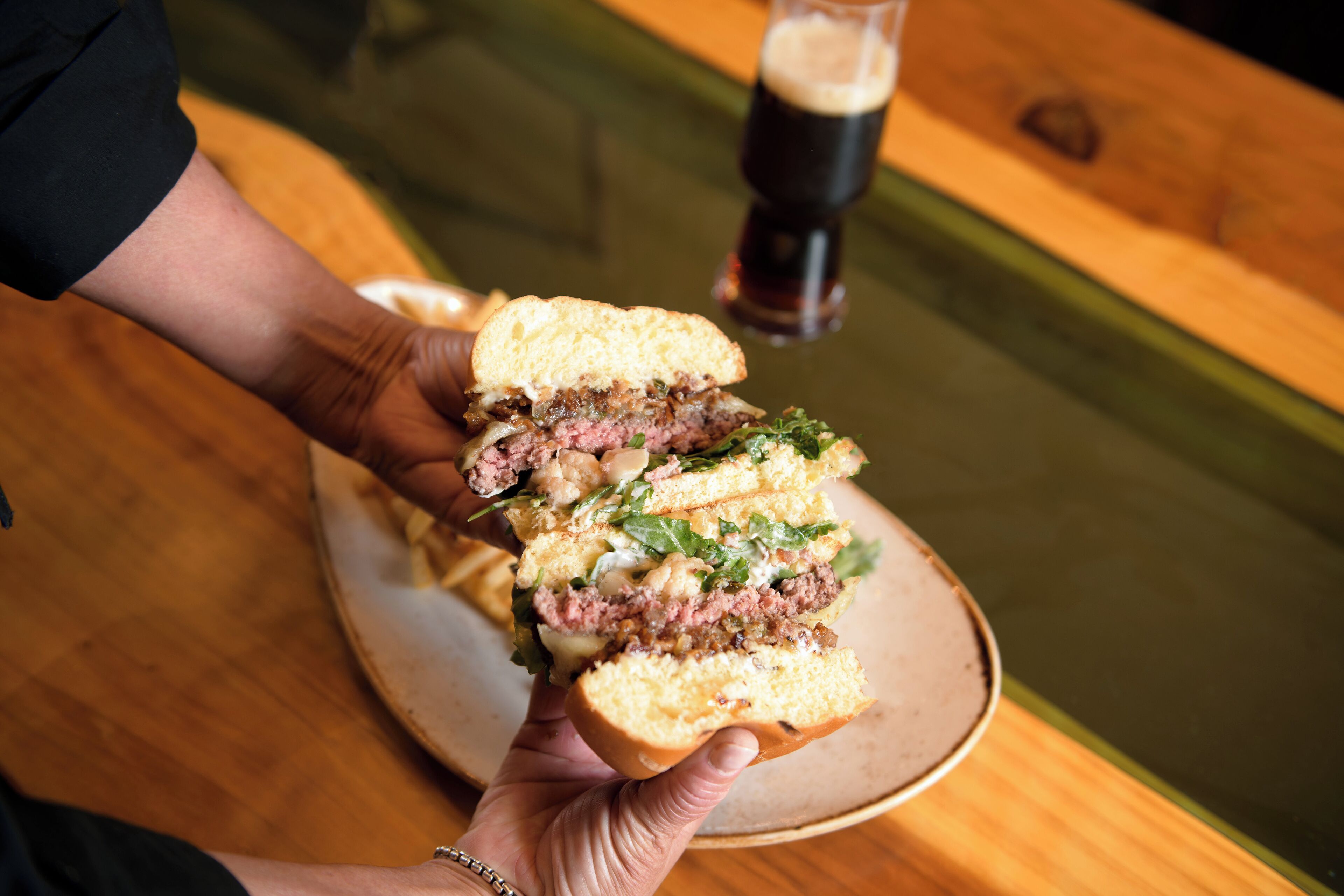 A person holding a sandwich with visible layers of meat, cheese, and greens.