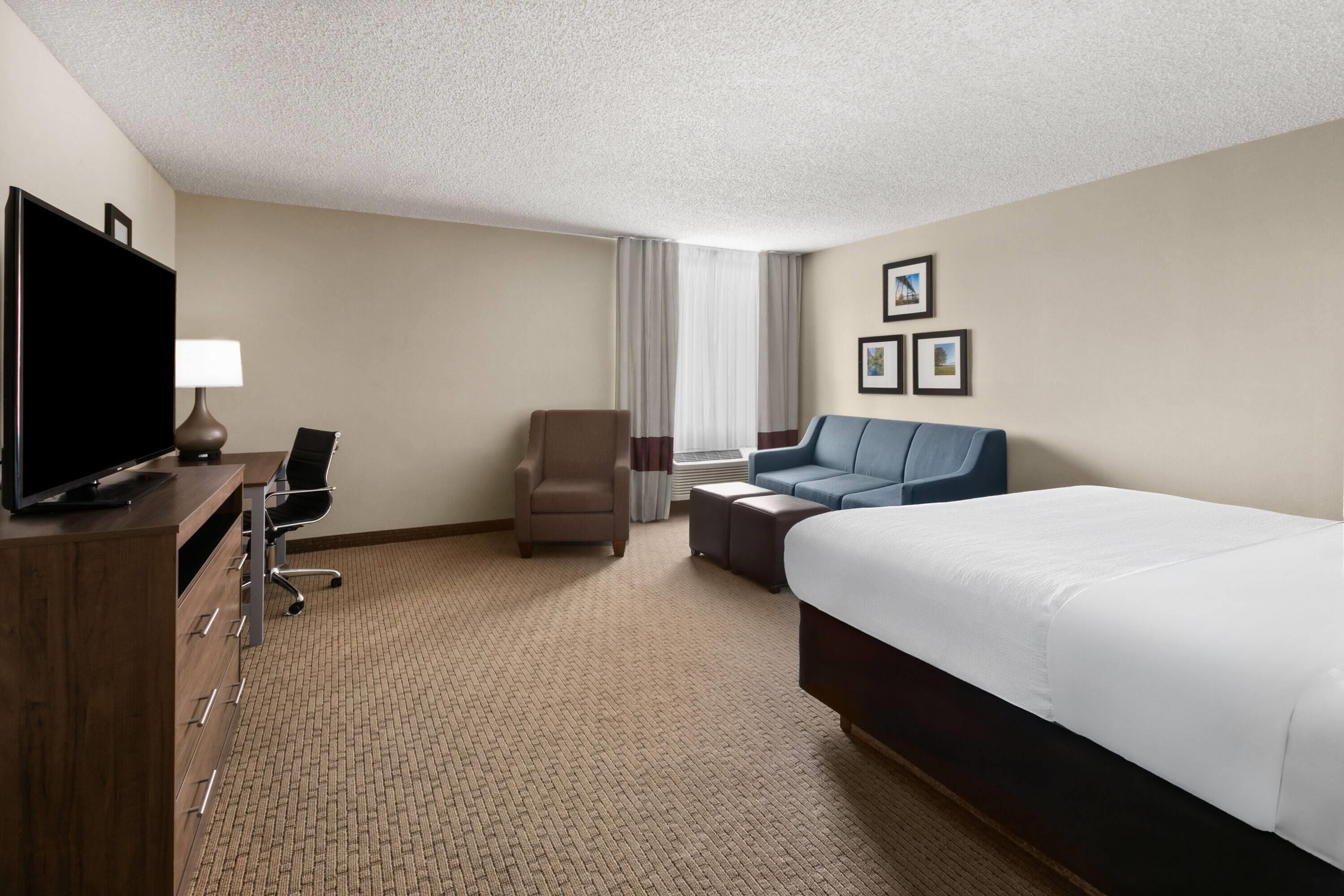 A hotel room with a bed, a desk with a chair, a television, and a sofa.