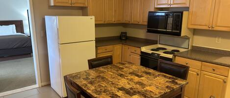 A compact kitchen with wooden cabinets, a refrigerator, a microwave, and a stove.
