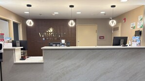 A reception area with a marble counter, a wooden wall with the Wingate logo, a door, and a computer monitor. - Wingate by Wyndham Utica (Utica)