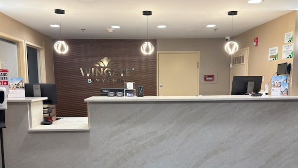A reception area with a marble counter, a wooden wall with the Wingate logo, a door, and a computer monitor.