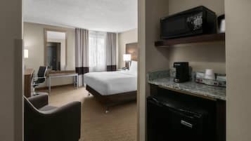 Habitación de hotel con cama, escritorio, silla, microondas, cafetera y refrigerador pequeño.