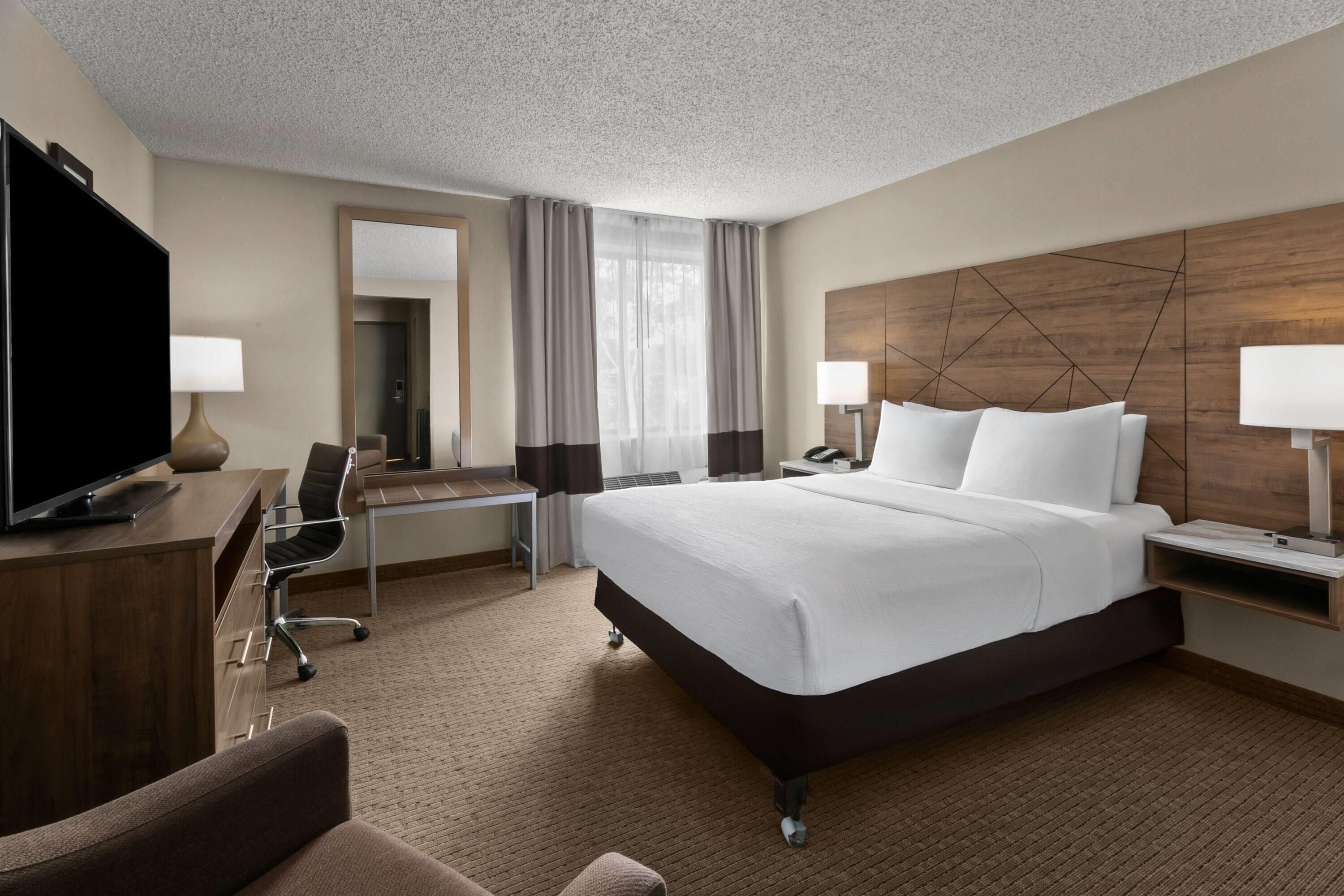 A hotel room with a large bed, a desk with a chair, a television, and two bedside lamps.