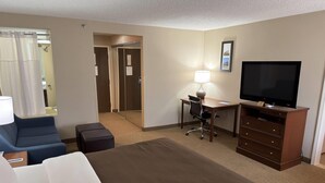 A hotel room with a bed, a desk with a chair, a television, a dresser, and a bathroom visible through an open door. - Wingate by Wyndham Utica (Utica)