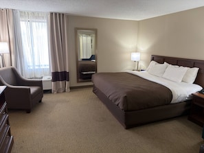 A hotel room with a large bed, a chair, a desk, and a mirror.