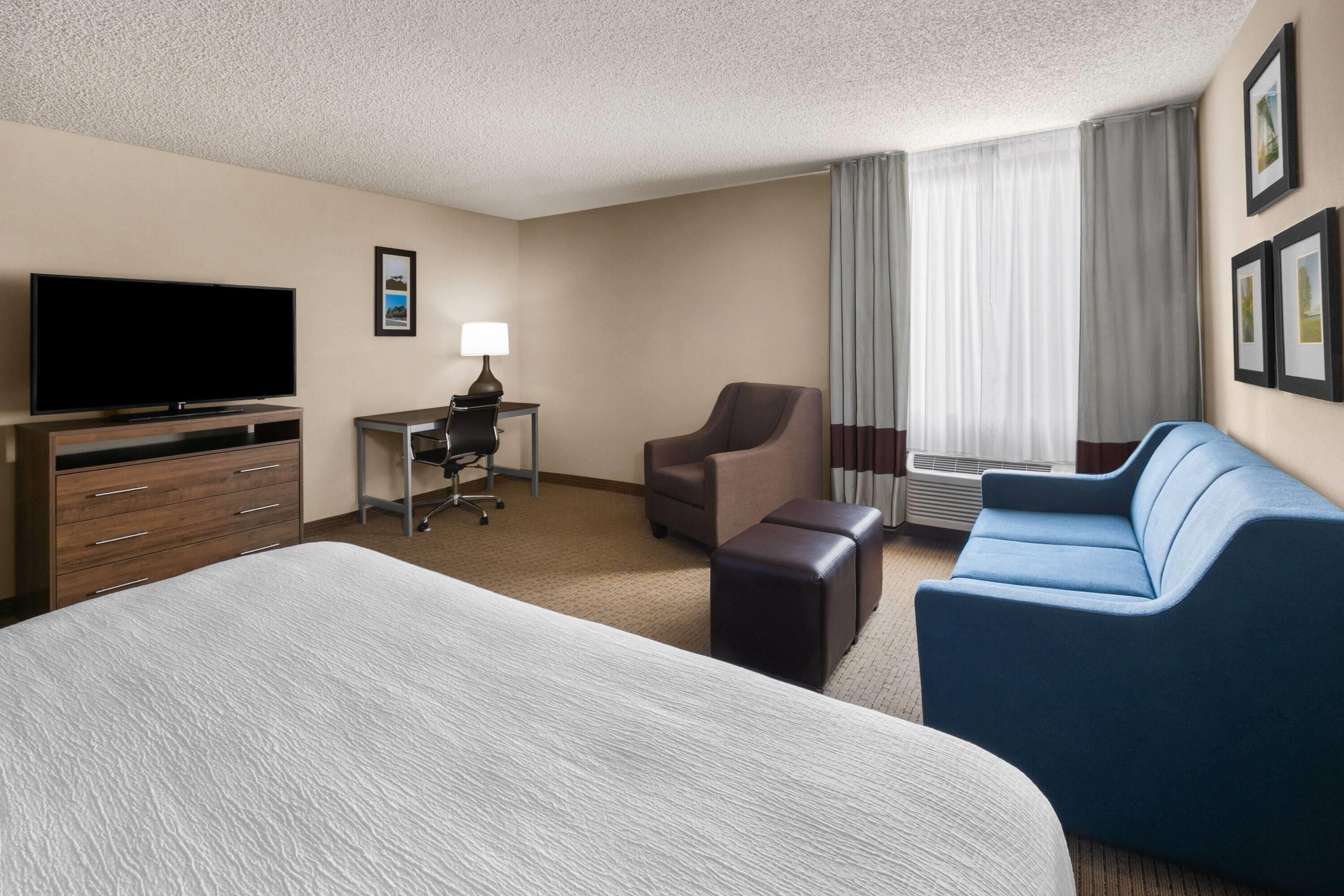 A hotel room with a large bed, a desk with a chair, a sofa, and a television.