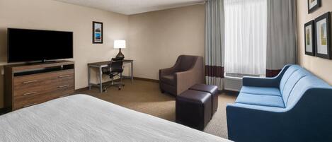 A hotel room with a large bed, a desk with a chair, a sofa, and a television.