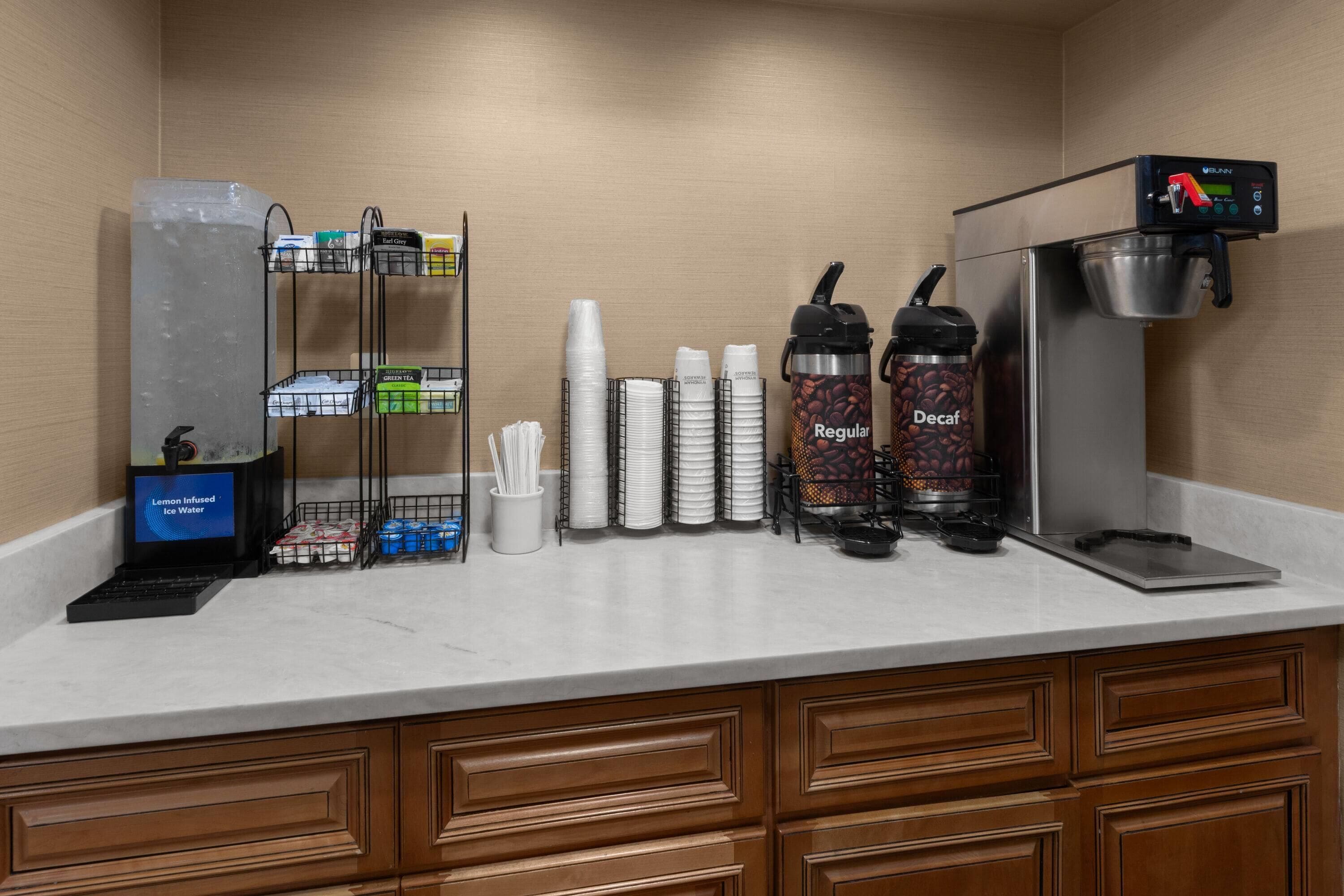 A self-service coffee station with a coffee machine, decaf and regular options, disposable cups, and a refrigerator.