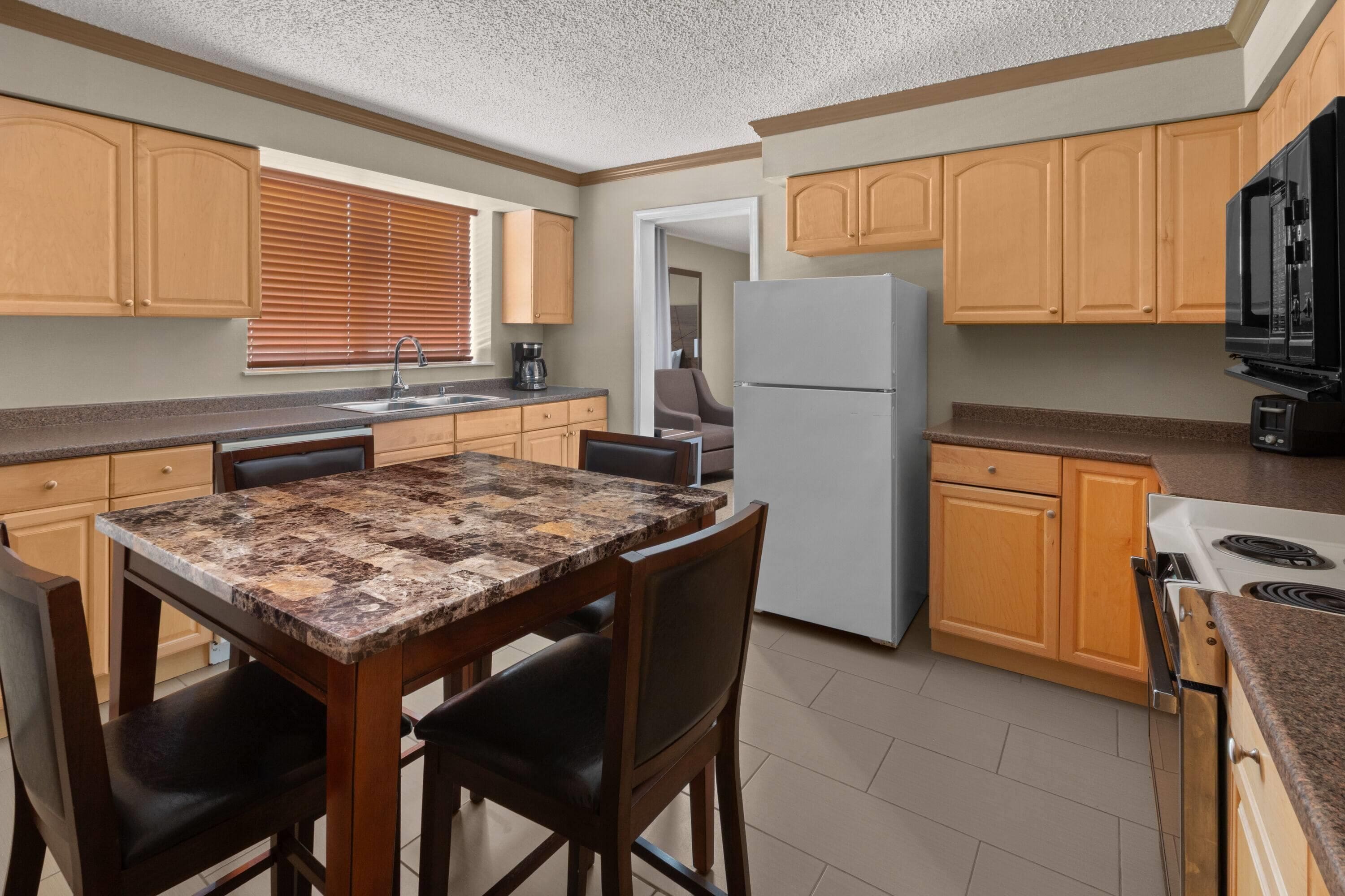A compact kitchen with wooden cabinets, a refrigerator, a stove, and a dining table with chairs.