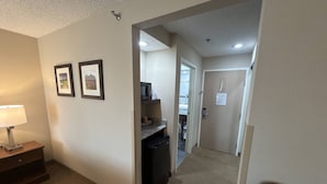 A hotel hallway with a lamp, framed pictures, a microwave, and a door with a sign.