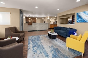 A hotel lobby with a reception desk, seating area, and a coffee machine.
