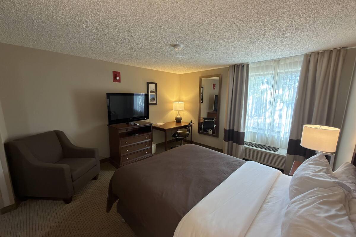 A hotel room with a bed, a TV, a desk, a chair, and a window with curtains.