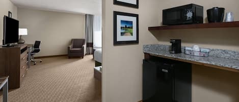 Habitación de hotel con kitchenette, televisión, escritorio, una silla y dos cuadros en la pared.
