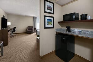 A hotel room with a kitchenette, a television, a desk, a chair, and two framed pictures on the wall.