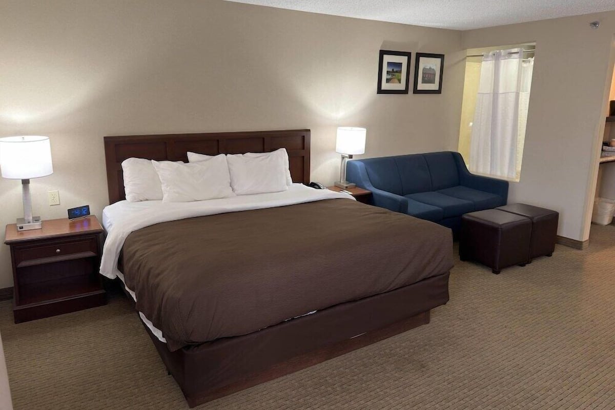 A hotel room with a large bed, bedside tables with lamps, a blue armchair, and a small side table.
