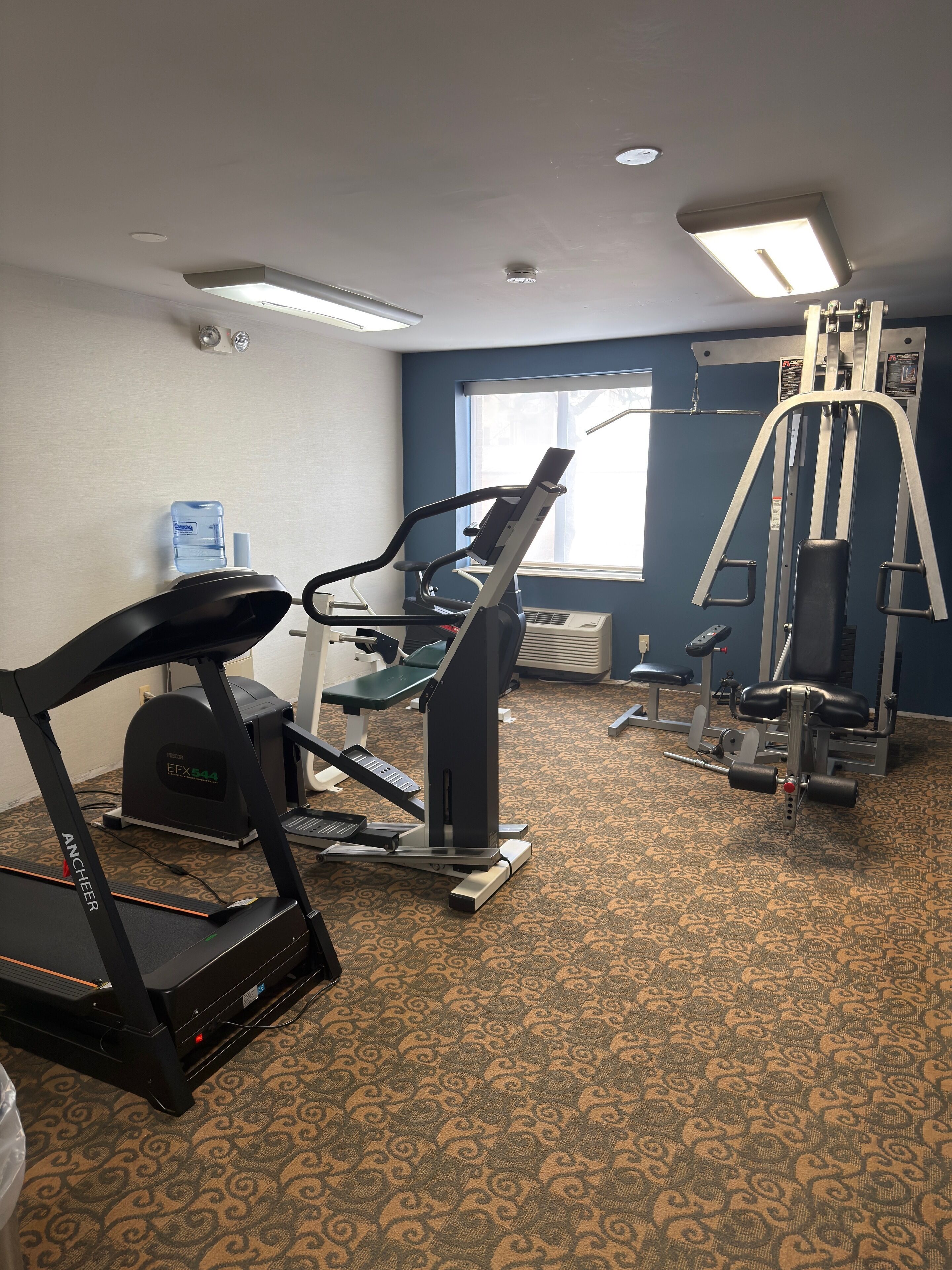 Ein Fitnessraum mit Laufband, Crosstrainer und Krafttrainingsgeräten.