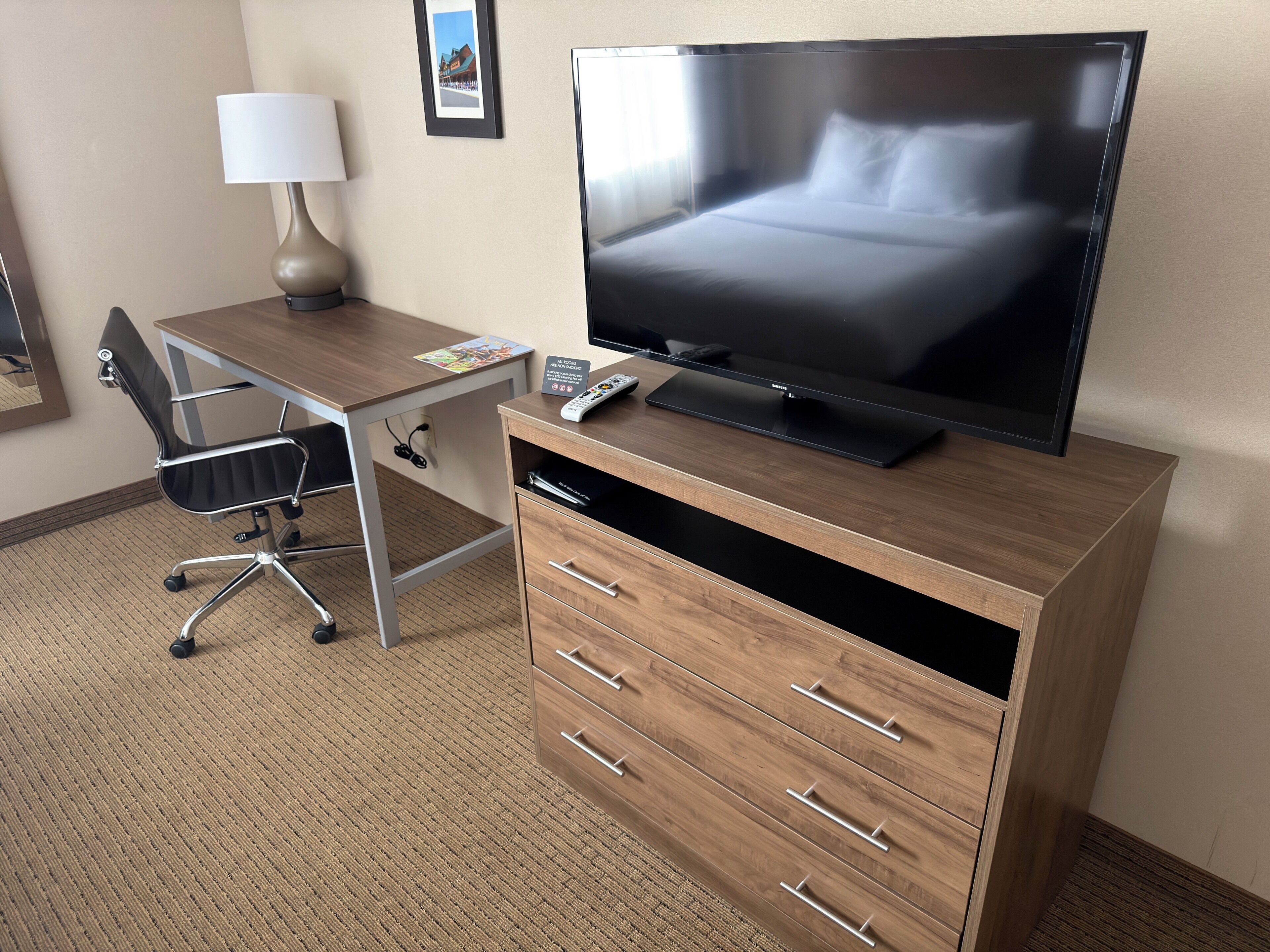 Une chambre d’hôtel avec un bureau en bois, un téléviseur à écran plat, une chaise, une lampe et un lit.