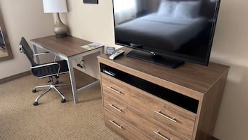 Une chambre d’hôtel avec un bureau en bois, un téléviseur à écran plat, une chaise, une lampe et un lit.