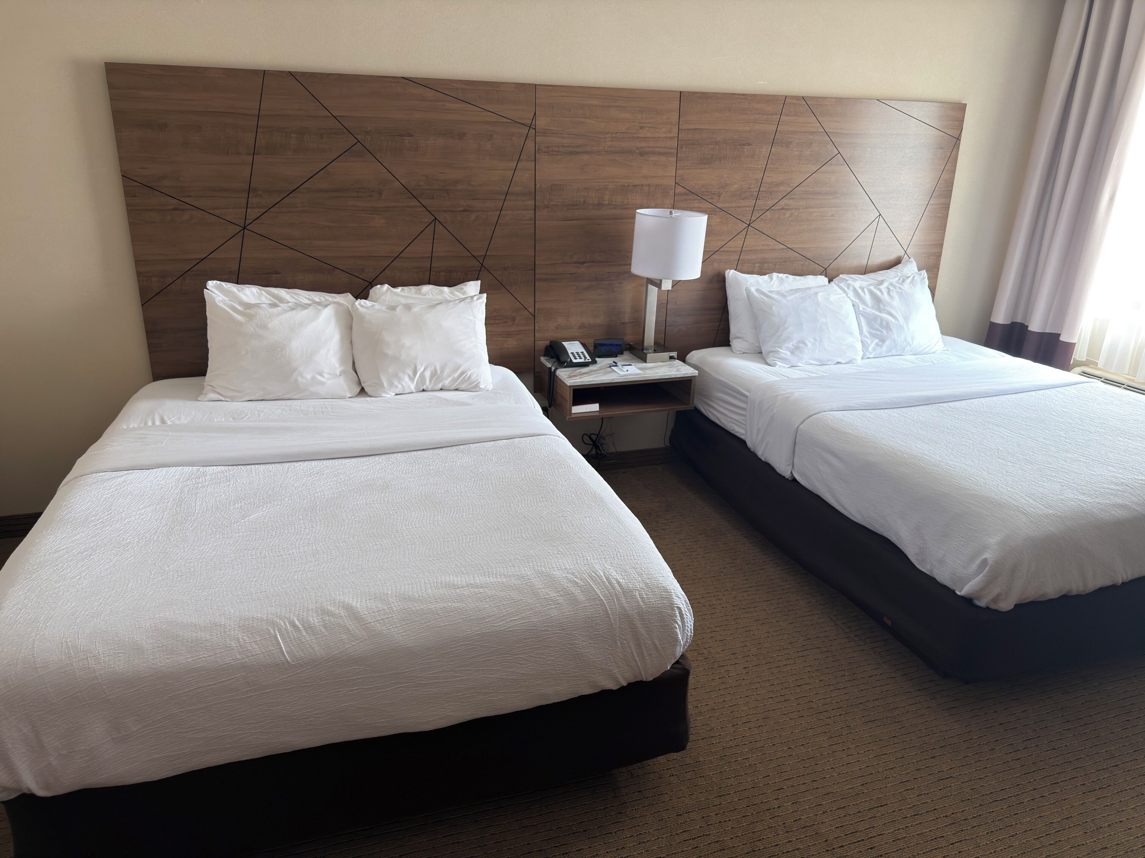 A hotel room with two beds, a nightstand with a lamp, and a wooden headboard.