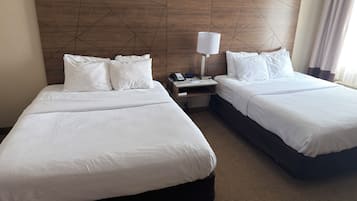 A hotel room with two beds, a nightstand with a lamp, and a wooden headboard.